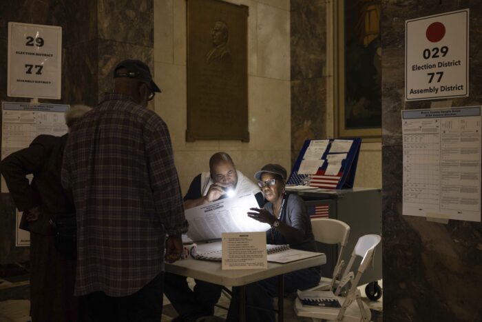 Two poll workers sitting at a table shine a flashlight on a ballot